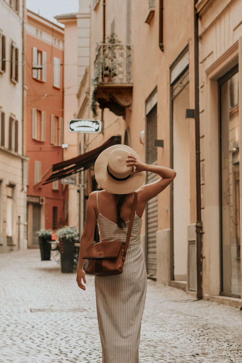 Vrouw lopend door italiaanse straatjes met een beige jurk en zomerse hoed