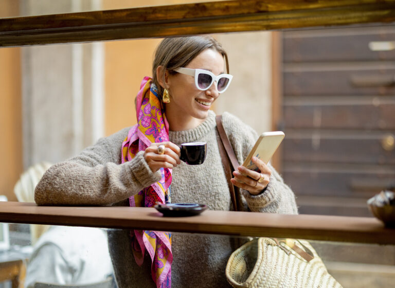 Vrouw kijkend op haar telefoon in italie met zonnebril op in de zomer drinkt espresso