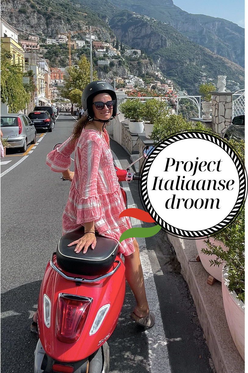 Liesbeth op een rode Vespa lachend op straat met rode jurk en helm op