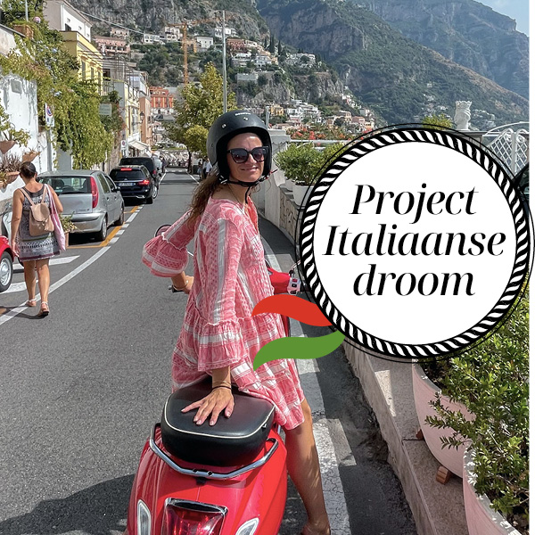 Liesbeth op een rode Vespa lachend op straat met rode jurk en helm op